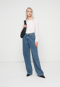 Camicia button-up rosa chiaro, pantaloni a gamba larga in denim blu morbidi, tacchi a punta nera e una piccola borsa nera. Texture lisce e stile casual.