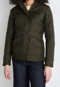 Olive green quilted jacket with a zip and snap closure, featuring two front pockets and a hood. Made from lightweight, textured fabric.