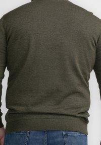 Man wearing olive green sweater and blue jeans, shown from the back against a plain white background.