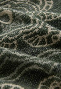 Green and beige patterned fabric with a textured weave, featuring swirling designs, enhancing visual complexity and depth.