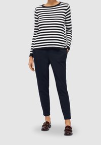 Haut à manches longues en coton rayé noir et blanc, associé à un pantalon bleu marine et des mocassins marron avec des accents dorés.