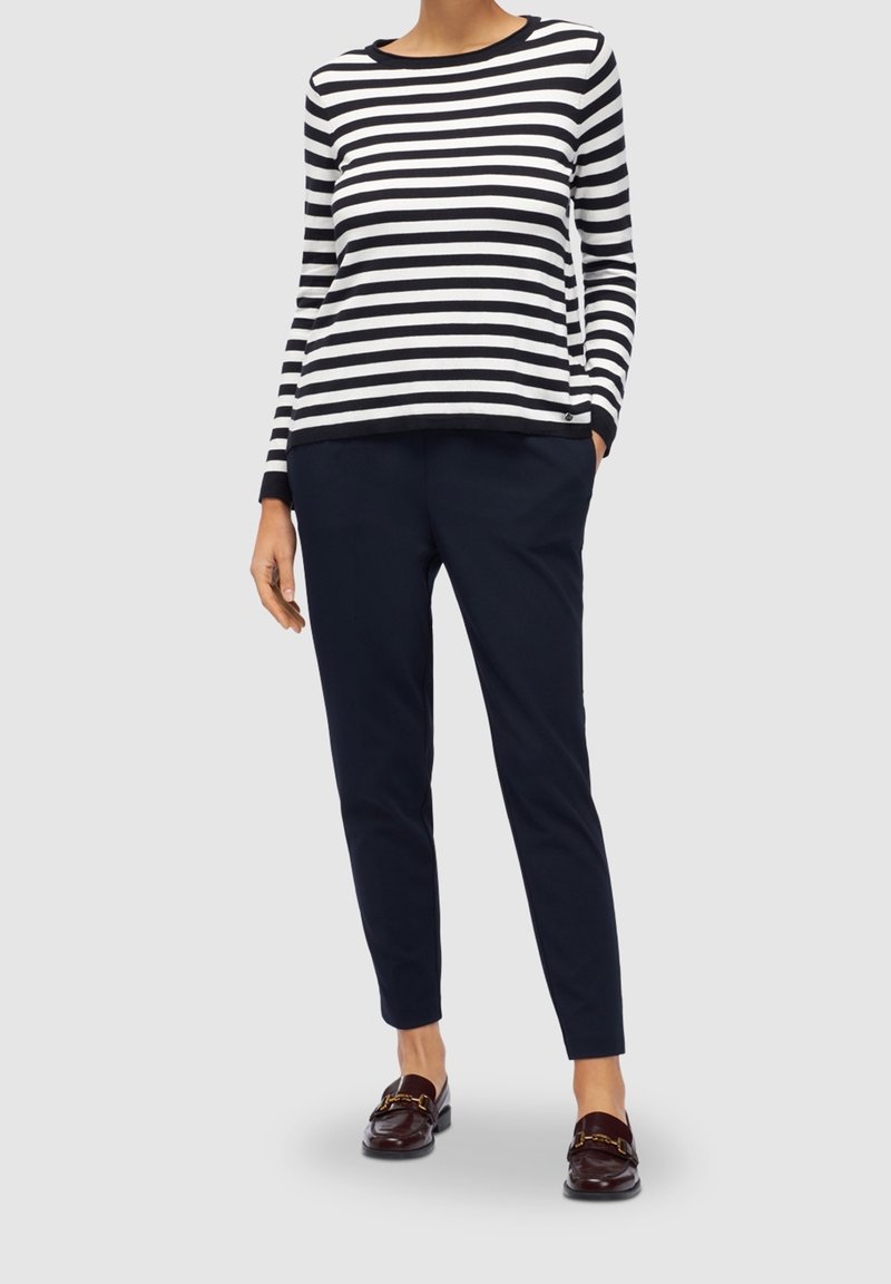 Haut à manches longues en coton rayé noir et blanc, associé à un pantalon bleu marine et des mocassins marron avec des accents dorés.