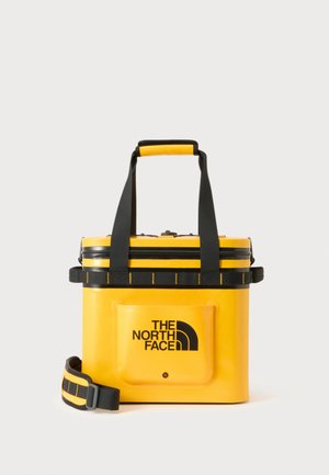 Bolsa nevera rígida amarilla con asas y correa negras, con el logo de The North Face en el bolsillo delantero sobre fondo blanco.