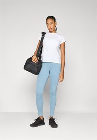 Svart treningsbag, hvit t-skjorte med korte ermer og lys blå leggings. Sorte joggesko med strukturert mønster. Enkelt design, tettsittende silhuett.