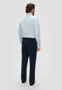 Lichtblauw gestreept shirt met lange mouwen, gecombineerd met donkerblauwe broek en witte sneakers. Voorzien van knoopzakken op de achterkant van de broek.