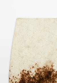 Jupe en tissu blanc cassé avec un motif tie-dye marron concentré en bas.