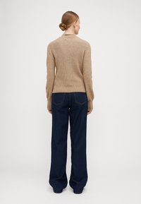 Beige, ribbestrikket genser med høy krage, kombinert med mørkeblå, vide denim-bukser med baklommer og kontraststing.