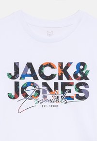 Hvit t-skjorte med fargerik, fet tekst som leser "JACK & JONES Essentials" med "EST. 1990" under grafikken.