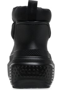 Botín negro impermeable con parte superior acolchada, material sintético texturado y suela de goma con puntos que presenta el logo de la marca.