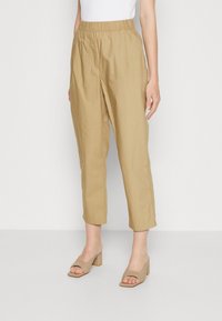 Una donna che indossa pantaloni beige a vita alta cropped con una cintura elastica, abbinati a sandali con tacco a blocco beige e aperti all'alluce.