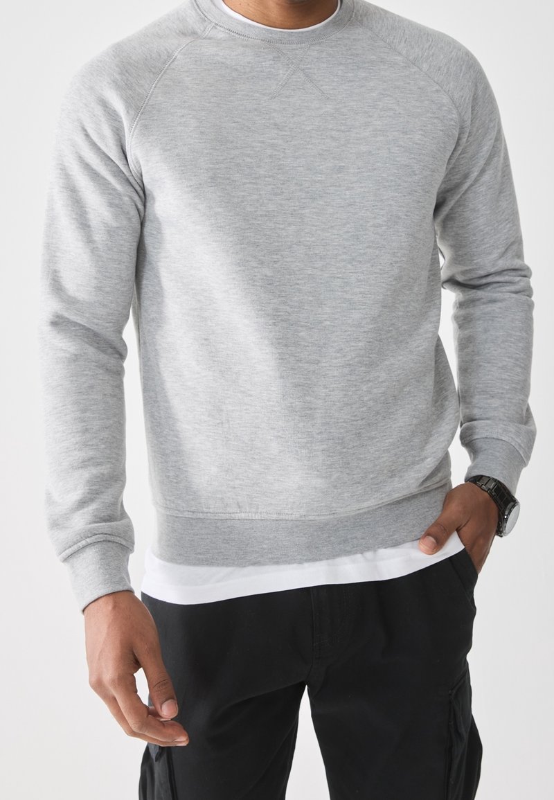 Harmaa puuvillane sweatshirt, millel on ümmargune kaelus, soonikkoes varrukad ja äär. Kandmine valge särgi peal, lõdva sobivuse ja sileda tekstuuriga.