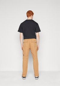 Czarny t-shirt i khaki spodnie cargo z kieszeniami i logo. Spodnie mają prosty krój i miękką fakturę, uzupełniając swobodny wygląd.