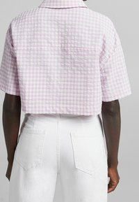 Kortärmad croppad skjorta i ljuslila och vit skotskrutigt mönster, med en texturerad tygkvalitet och klassisk krage, matchad med vita byxor.