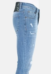 Smalle blauwe spijkerbroek met beschadigde details, een zwart logo-opdruk op de achterkant en een klassieke vijf-pocket ontwerp.