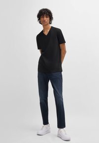 Tricou negru cu mânecă scurtă, de tip v-neck, asortat cu blugi negri și adidași albi. Material neted cu o croială lejeră, fără modele vizibile.