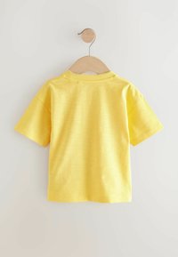 Kortærmet gul T-shirt lavet af blødt stof, med en rund halsudskæring med ribkant og en glat tekstur. Hængende på en træholder.