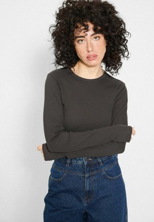 Ciemnoszara prążkowana bluzka z długimi rękawami i okrągłym dekoltem, połączona z niebieskimi jeansami o wysokim stanie z kieszeniami z przodu i zapięciem na guziki.