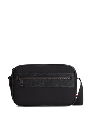 Black crossbody bag with front zip pocket, textured strip, adjustable strap, and small red, white, and blue detail on the side.