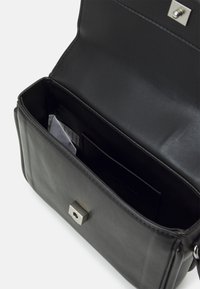 Svart läderhandväska med rektangulär form, utrustad med magnetknäppning och inre fickor för organisering. Slät yta.