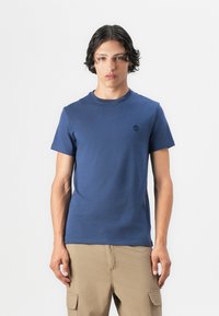 Tricou bleu marin cu mânecă scurtă, realizat dintr-un material moale, având un guler rotund și un mic logo pe partea stângă a pieptului.