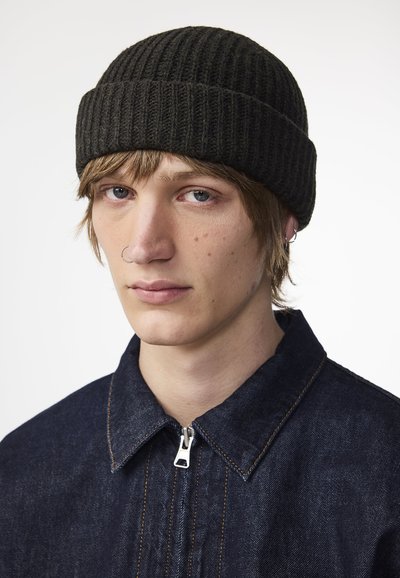 Beanie a coste scuro con una vestibilità aderente, indossato con una giacca in denim scuro con chiusura a zip e dettagli di cucitura arancione.