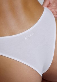 Culotte bikini en coton blanc à la texture douce, présentant une coupe taille basse et un logo discret sur la ceinture.