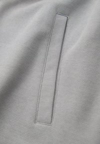 Tejido gris texturizado con un bolsillo rectangular de bordes reforzados, que muestra un sutil patrón tejido.