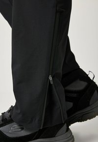 Pantalones exteriores negros con puños con cremallera, hechos de tela suave. Combinados con zapatos resistentes en negro y gris con acentos de malla.