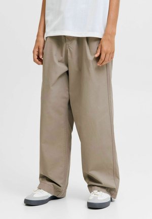 Child wearing loose beige pants, white sneakers with gray soles, and a white top against a plain light background.