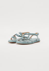 Sandales en suédine bleue avec un design de sangle tissée, ornées de strass bleu clair, dotées d'une semelle plate et de brides de cheville réglables.