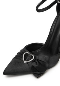 Pantof cu toc înalt din satin negru, cu vârf ascuțit, având un detaliu din material plisat și un accent din stras în formă de inimă.