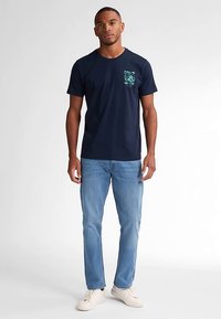 Tmavě modré bavlněné tričko s krátkými rukávy a potiskem na hrudi. Kombinováno s světle modrými džínami a bílými teniskami.