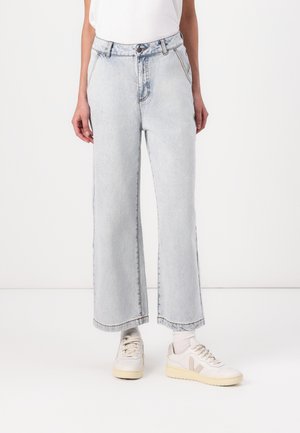 Light blue high-waisted wide-leg jeans with frayed hem, made of denim, featuring a buttoned fly and five-pocket design, paired with white sneakers.