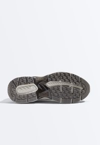 Kenkäpohja, jossa monisuuntainen kulutuspintakuvio harmaana ja mustana, jaossa olevat pitoalueet sekä teksturoitu kumipinta pidon takaamiseksi.