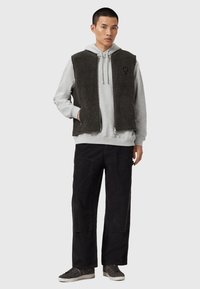 Un gilet en fourrure noire sur un sweat à capuche gris, associé à un pantalon large en velours côtelé noir et des baskets grises. Matériaux texturés avec un design décontracté.