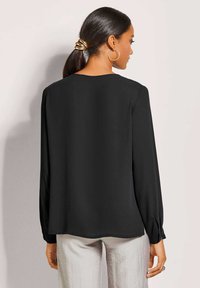 Zwarte blouse met lange mouwen en een ronde halslijn, van gladde stof met gathered manchetten, gecombineerd met lichtgekleurde broek. Eenvoudig ontwerp, geen patronen.
