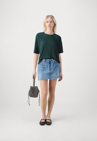 Grønn ribbet t-skjorte med korte ermer, lyseblå denimskjørt med frayed hem, svarte naglede leiligheter, og en mønstrete bøtteveske.