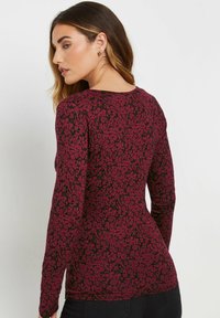 Langärmliges Oberteil in Burgunderrot mit einem schwarzen Blumenmuster, aus einem weichen, dehnbaren Stoff gefertigt. Verfügt über einen runden Ausschnitt und eine taillierte Silhouette.