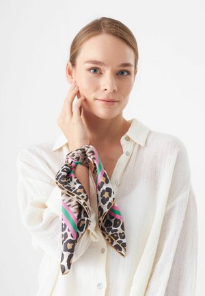 Leopardenprint zijden sjaal met roze en groene strepen, geknoopt om de pols. Model draagt een witte, lichte knoopshirt.