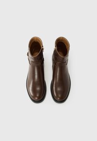 Bottes chelsea en cuir marron avec une texture lisse, des zips sur les côtés et un panneau à motif contrastant. Semelles en caoutchouc noir, design à bout rond.
