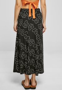 Black midi skirt featuring white floral patterns, made from a soft fabric with an elastic waistband. Paired with brown slide sandals.