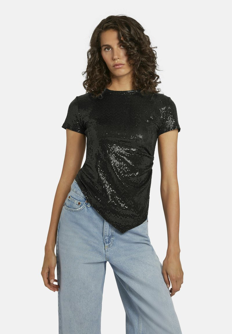 Zwarte t-shirt met pailletten, fitted design, korte mouwen en een afgeronde onderkant, gecombineerd met lichtblauwe wijde jeans.