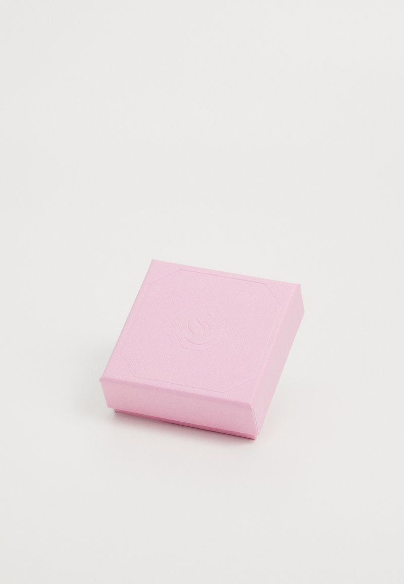 Petite boîte carrée rose fermée avec logo en relief sur le couvercle, posée sur une surface blanche unie.