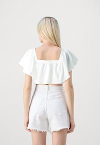 Blouse blanche raccourcie avec des manches à volants et un col carré ; présente des détails en œillet. Associée à des shorts blancs effilochés taille haute.