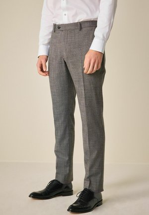 Pantalones de cuadros grises con un corte entallado, que cuentan con un frente plano, bolsillos laterales y cierre de botón en la parte delantera, combinados con zapatos de piel negros.