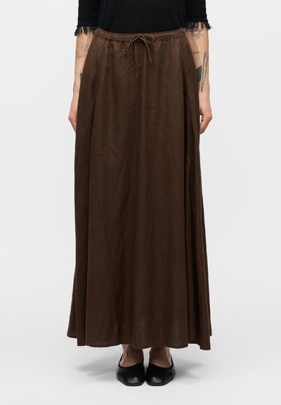 Jupe longue marron avec une taille à cordon, faite d'un matériau léger. Elle présente une texture lisse et tombe jusqu'à la cheville. Chaussures plates noires portées.