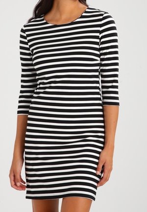 Femme portant une robe à rayures horizontales noires et blanches avec des manches trois-quarts et un col rond.