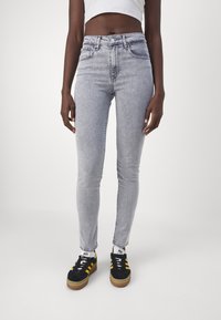 Grå högmidjade skinny jeans med en blekt finish, med knappstängning fram och fem fickor, i kombination med svarta och gula skor.