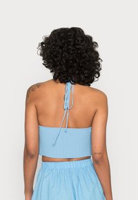 Top cropped em azul claro com textura estriada e design de atar nas costas, combinado com uma saia leve azul clara. Tecido ajustado.