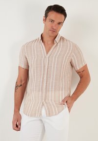 Camisa de manga corta, abotonada en beige con rayas verticales blancas, hecha de tela ligera, con un corte relajado y un cuello con muesca.